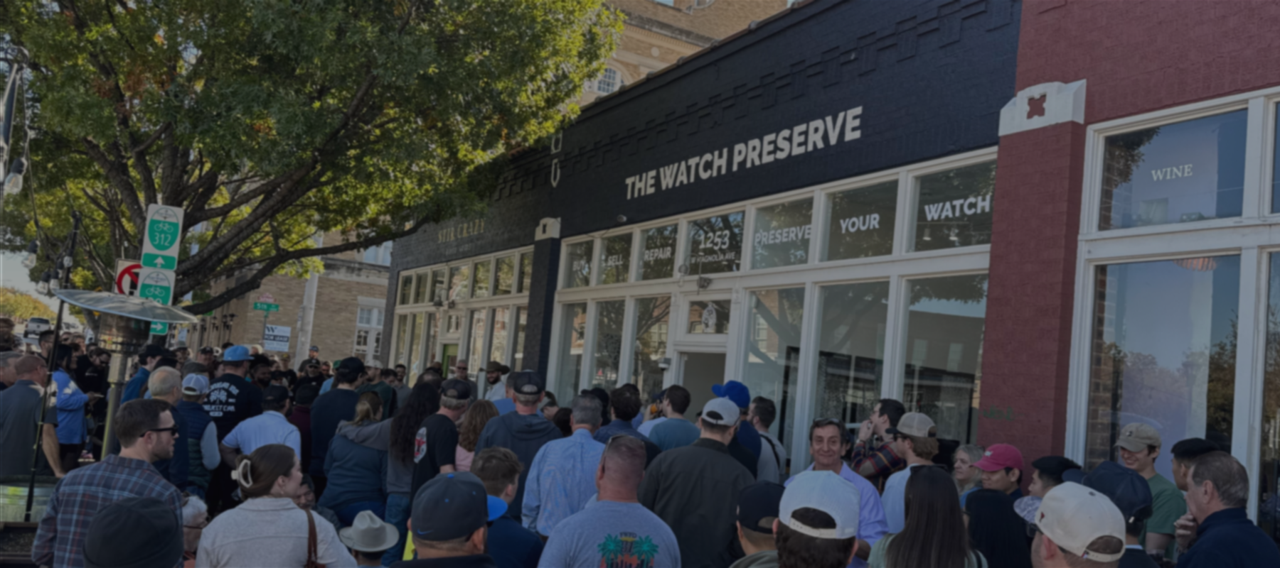 Crowd gathered outside 'The Watch Preserve' store on a sunny day.